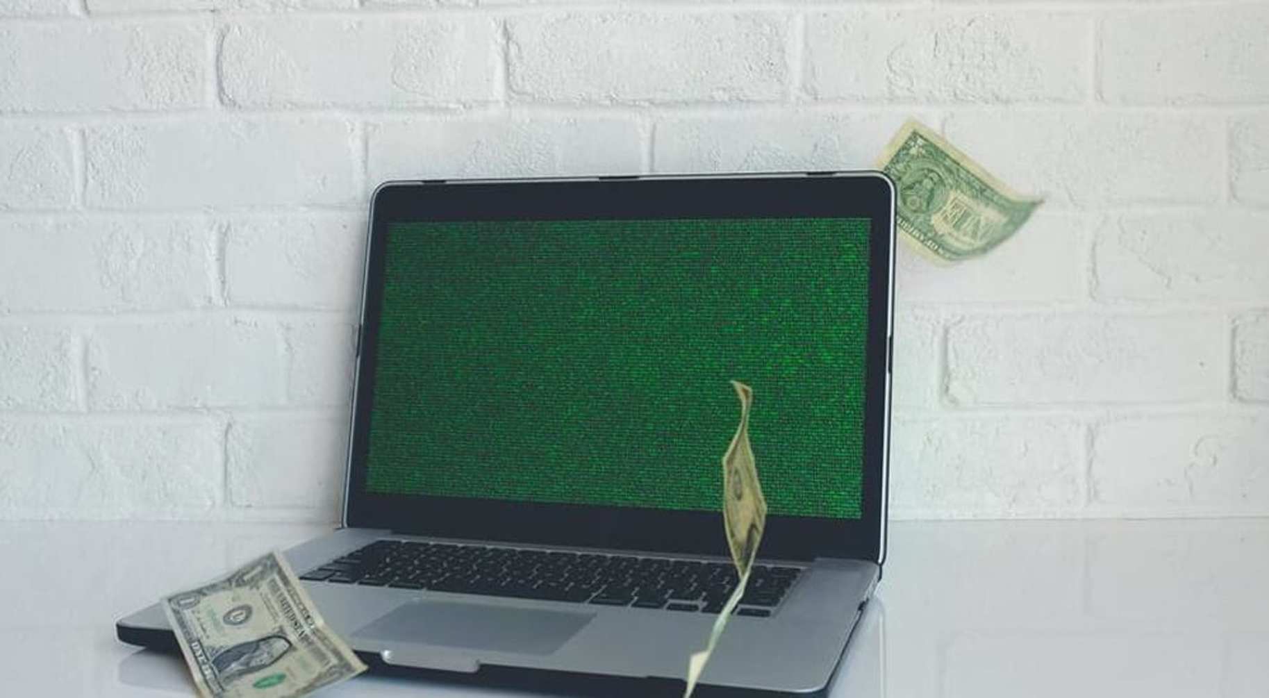 Dollar bills falling around an open laptop on a table